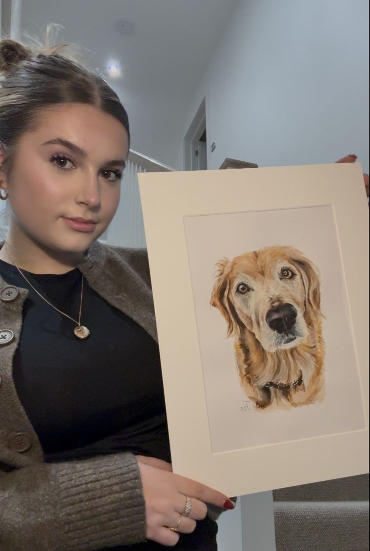 Jules Farrell holding a finished mounted watercolour portrait of a golden retriever